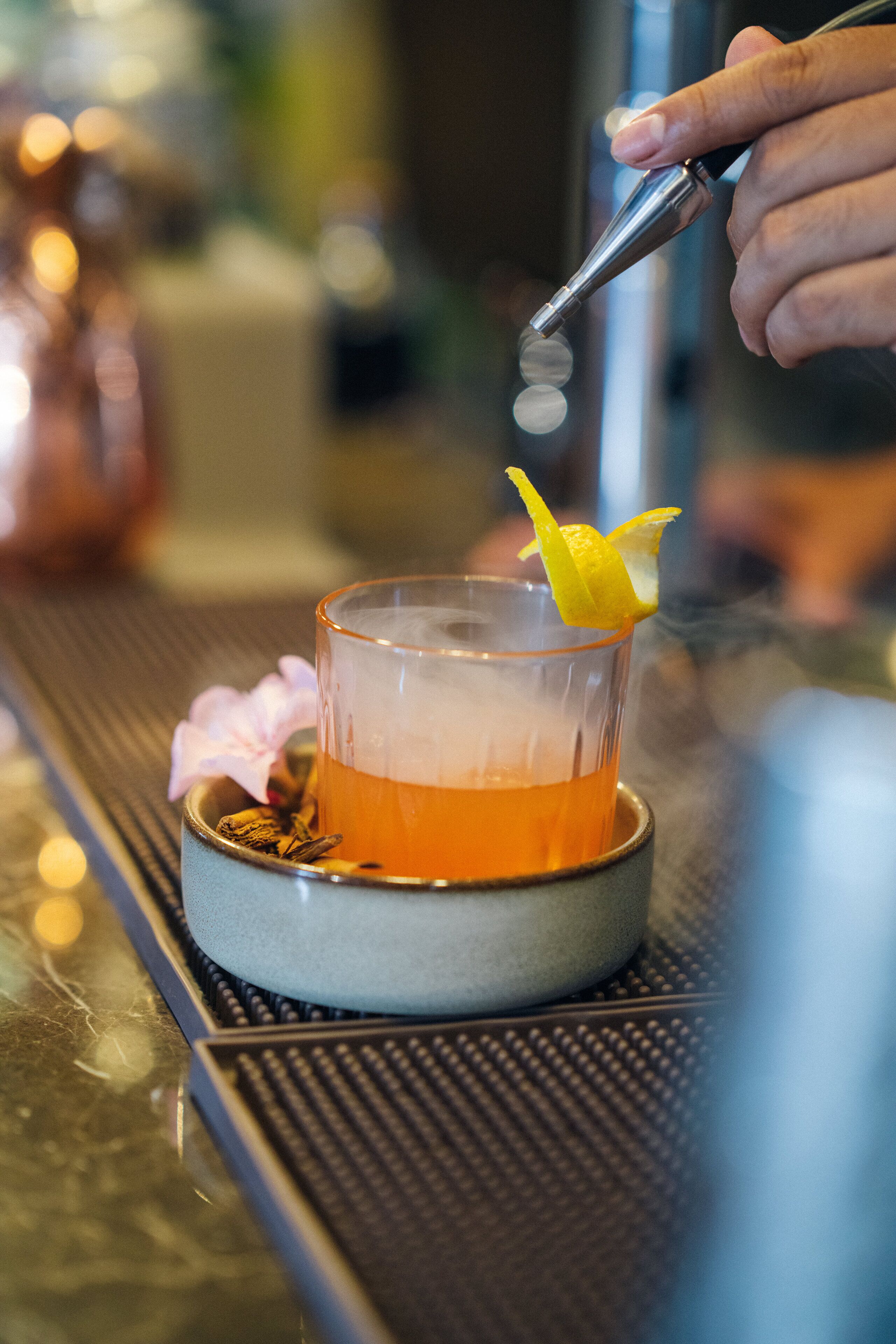 A cocktail being prepared with a lemon twist garnish.