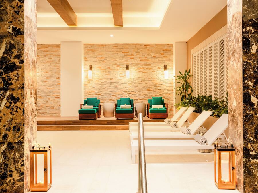 A spa area with stone walls, green cushioned chairs, and white loungers.