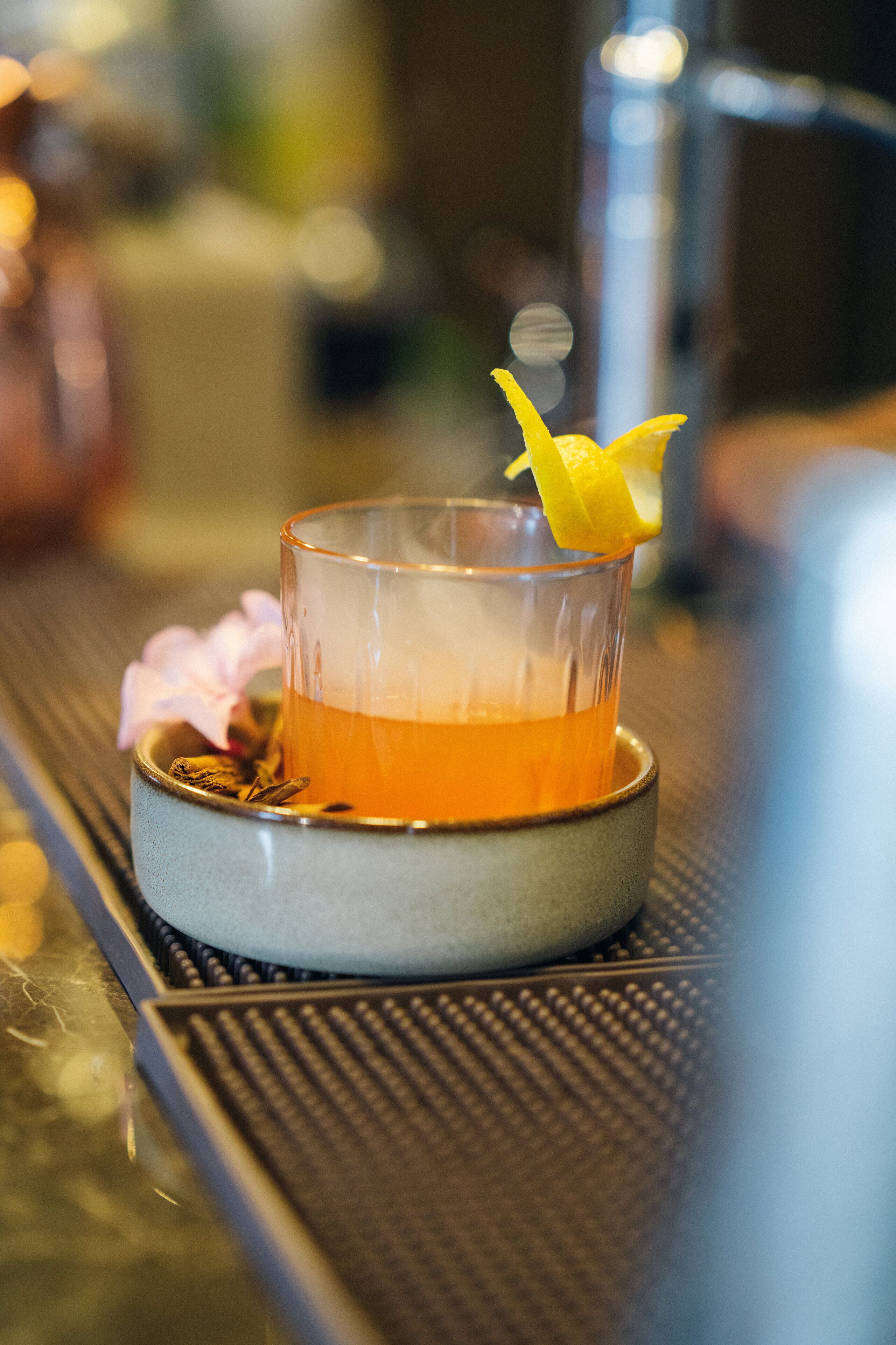 Un verre contenant un liquide ambré, garni d’une tranche de citron et posé sur un sous-verre, lui-même placé sur une surface texturée.