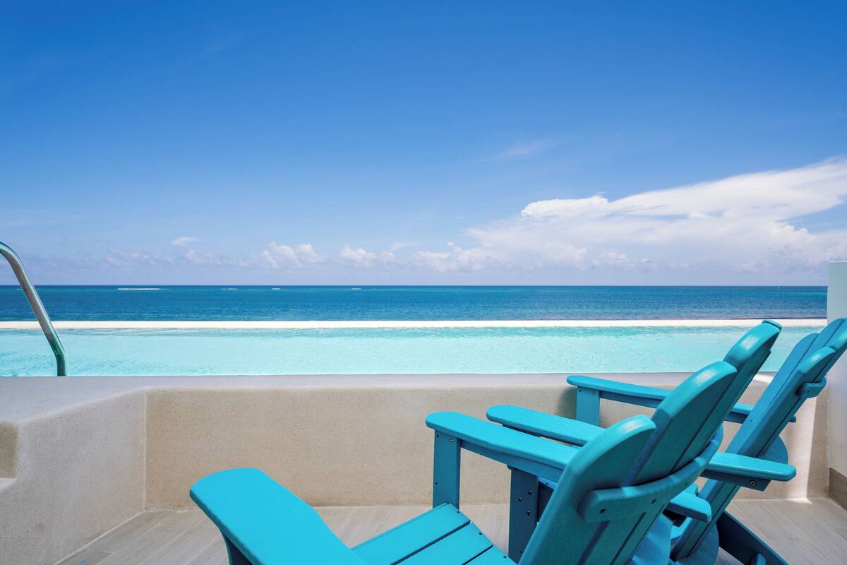 A poolside area with turquoise chairs and a view of the ocean.
