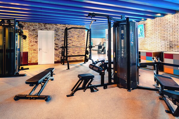 Ein Fitnessraum mit unterschiedlichen Trainingsgeräten, einer Bank und einer Tür.