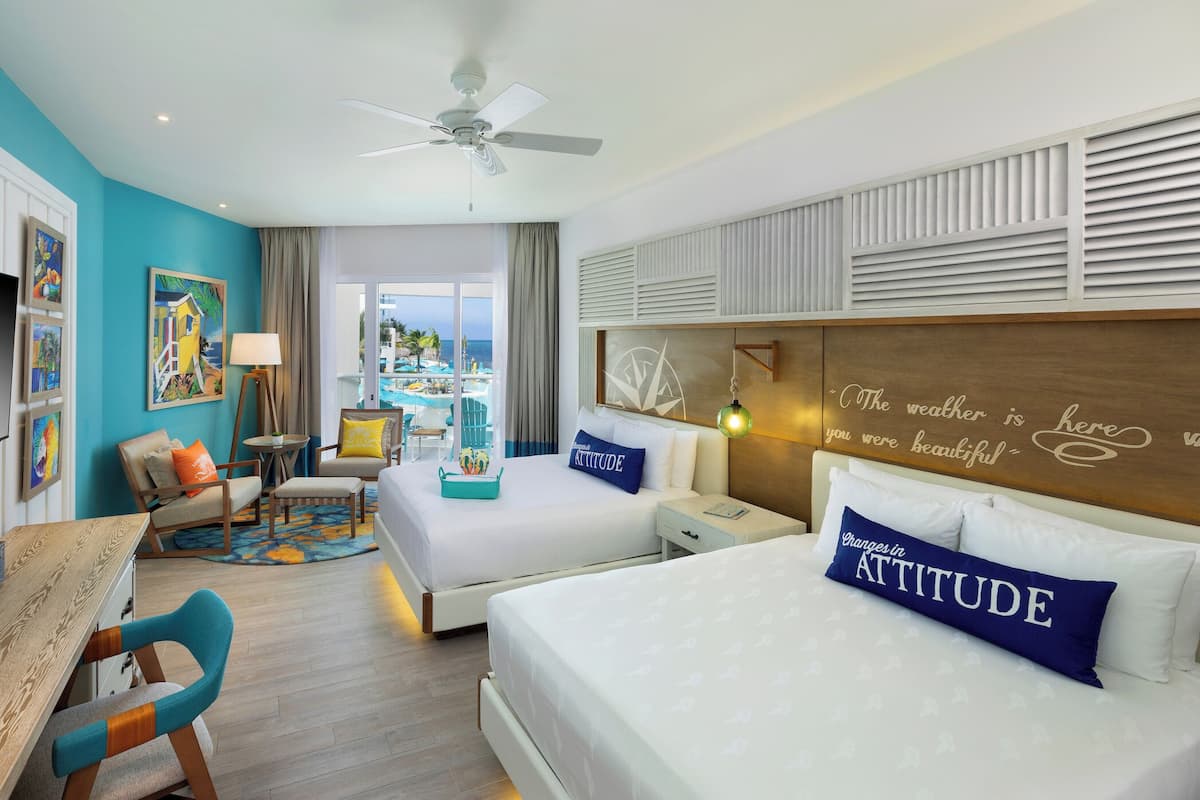 A hotel room with a bed, two chairs, a desk, a TV, and a view of the ocean.