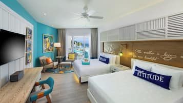 A hotel room with a bed, two chairs, a desk, a TV, and a view of the ocean.