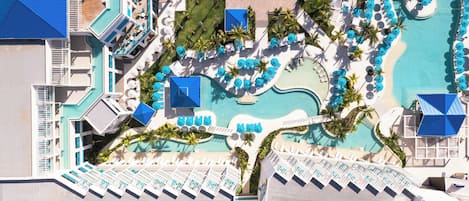 Vue aérienne d’un complexe hôtelier doté de plusieurs piscines, de chaises longues et de palmiers.