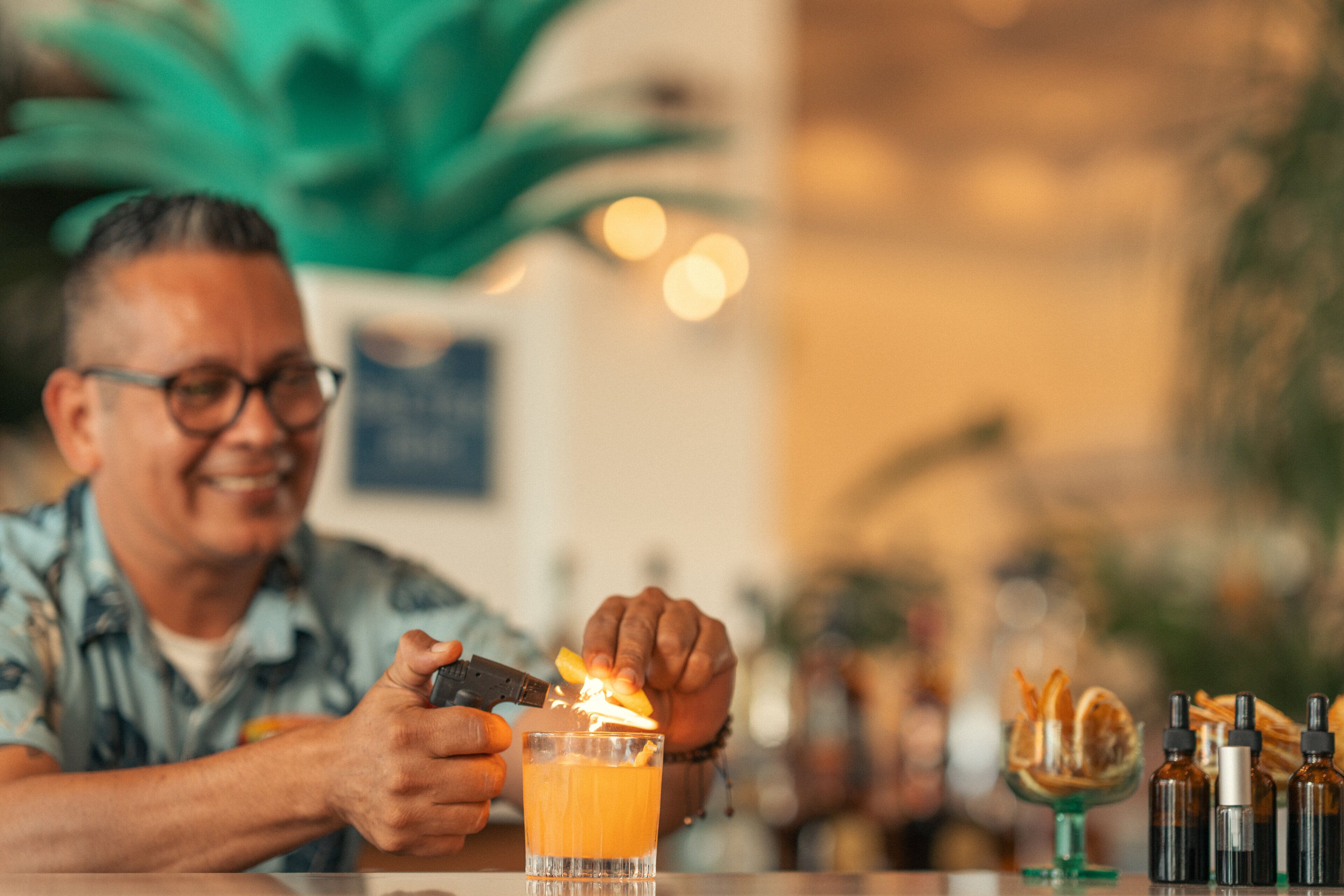 A person preparing a drink with a flaming orange peel in a glass.