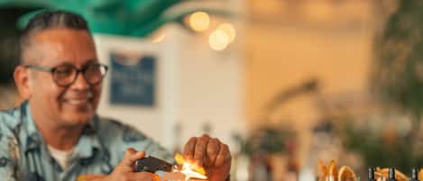 A person preparing a drink with a flaming orange peel in a glass.