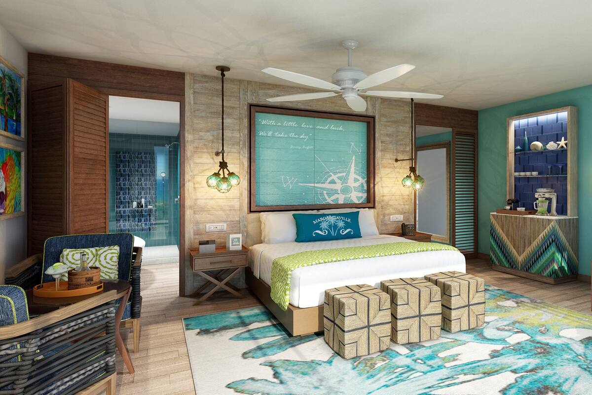 A well-lit bedroom with a large bed, a ceiling fan, a map on the wall, and a view of the sea through the window.