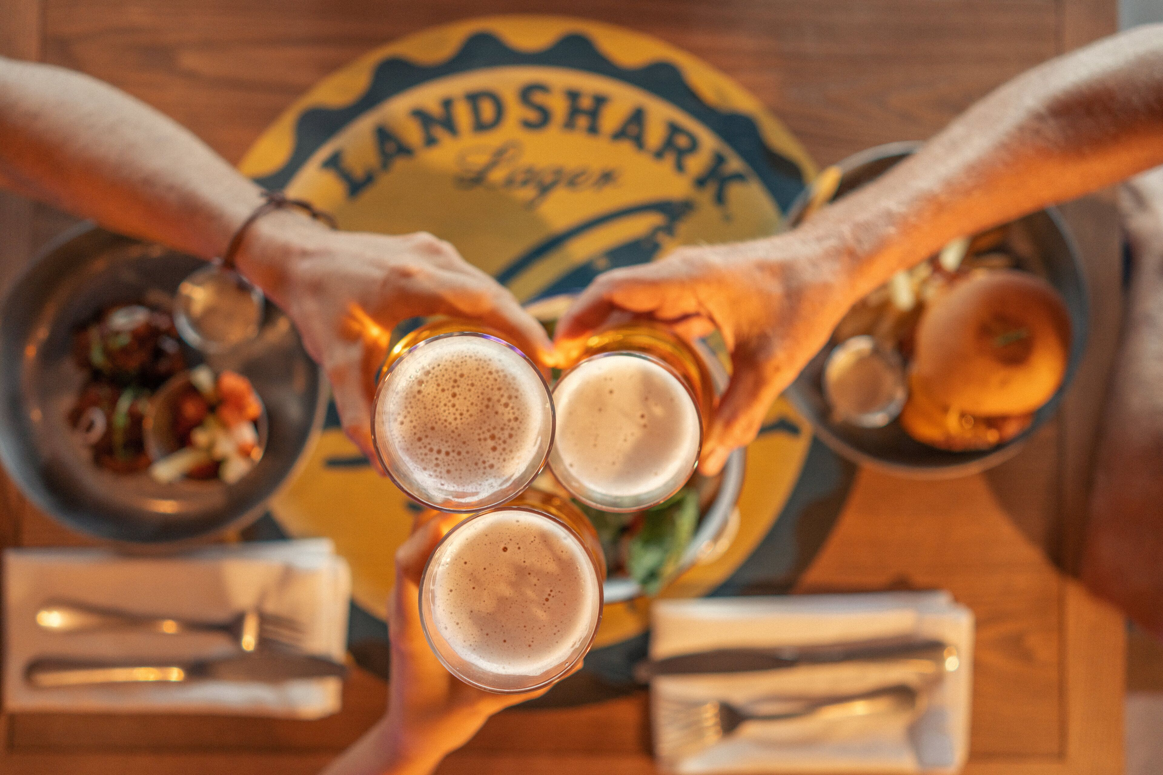 Three people toasting with glasses of beer in front of a sign that reads "LAND SHARK Lager."