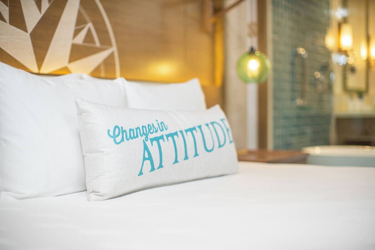 A bed with white bedding and a pillow with the text "Champions Attitude".