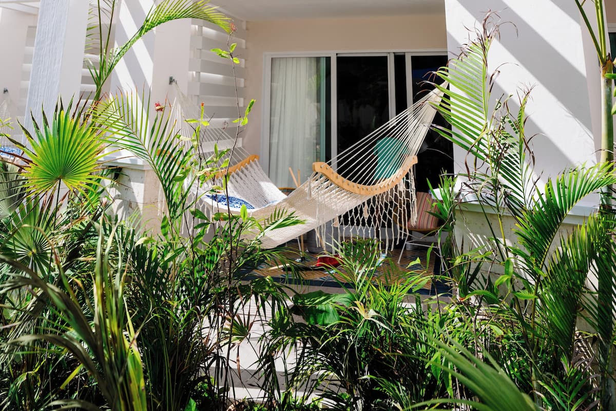 A modern building with a white exterior, a balcony with a hammock, and lush greenery.