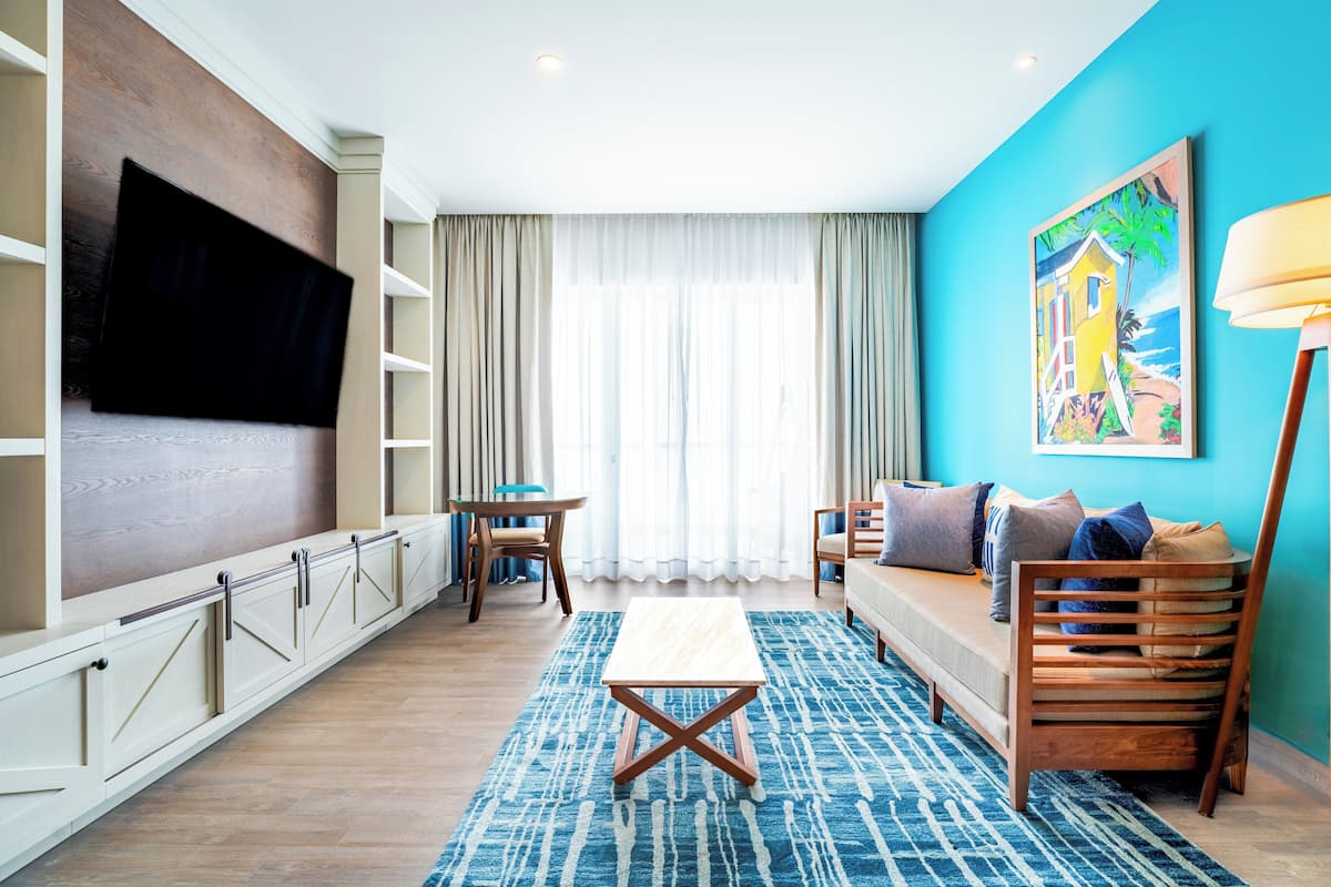 A modern living room with a flat-screen TV, wooden furniture, a blue accent wall, and a large window with sheer curtains.