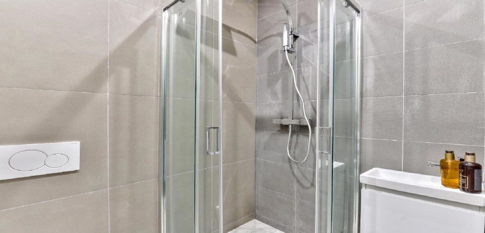 Een douche met glazen wanden, bedieningspaneel en een wit wastafelmeubel met toiletartikelen.