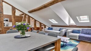 A modern loft apartment with exposed wooden beams, a dining area with a table and chairs, a sofa set, and a kitchen in the background. - A paradise for food lovers- An essence of French gastronomy in Montrogueil (Paris)