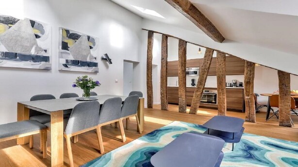 A modern dining area with a wooden table and grey chairs, a colorful rug, and abstract wall art. - A paradise for food lovers- An essence of French gastronomy in Montrogueil (Paris)
