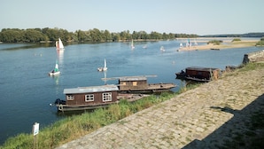 Vista al río con barcos, una casa flotante de madera y un muro de piedra.