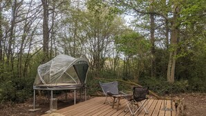 Un campamento con una tienda de campaña, dos sillas y una plataforma de madera en un bosque.
