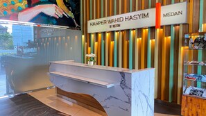 A reception desk with a marble top and a wooden base, flanked by vertical wooden slats with illuminated panels. - Harper Wahid Hasyim, Medan by Aston (Medan)