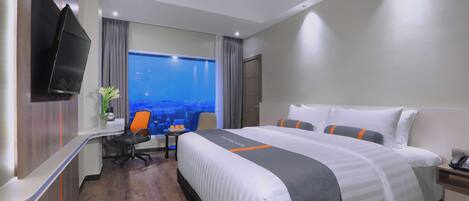 Une chambre d’hôtel avec un grand lit, un bureau, une chaise, une télévision et une fenêtre donnant sur la ville.