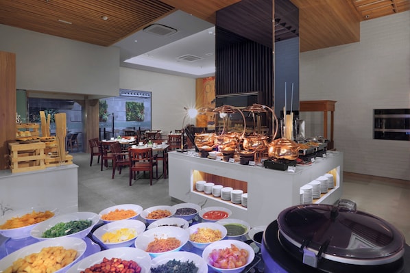 Buffet-alue, jossa on tarjolla monipuolinen valikoima ruokia, sekä ruokailualue, jossa on pöytiä ja tuoleja.