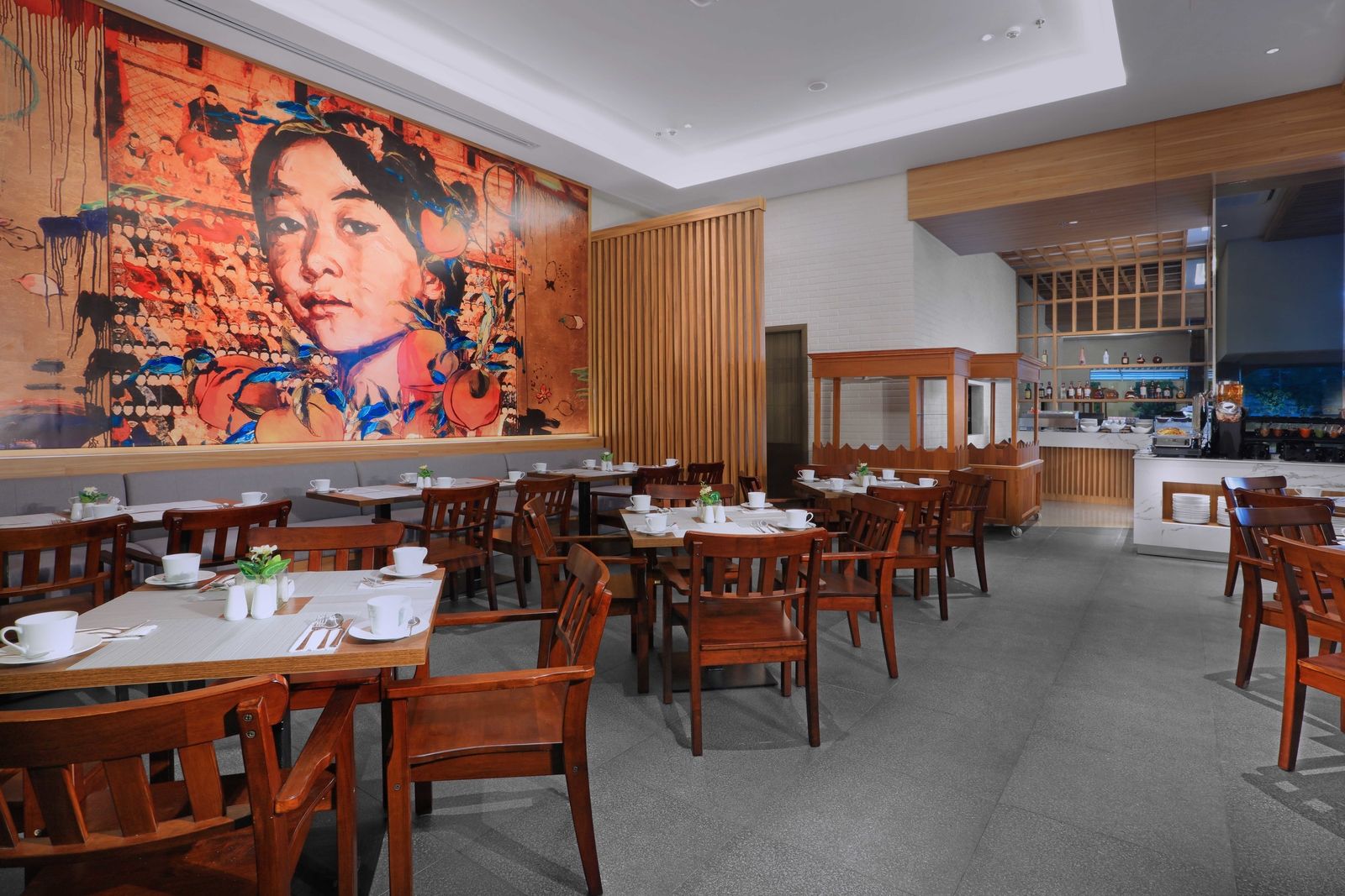 A restaurant with wooden tables and chairs, a large abstract painting on the wall, and a bar area in the background.