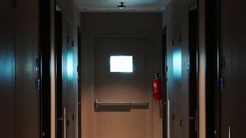 A narrow hallway with doors on both sides, a fire extinguisher on the right, and a small window at the end.