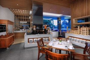 A modern restaurant with a central island, wooden furniture, and a view through large windows.