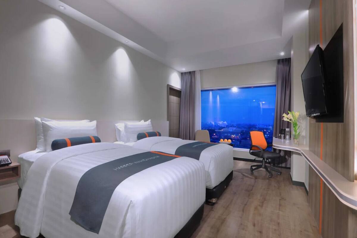 Hotellihuone, jossa on kaksi sänkyä, työpöytä, televisio ja näkymä kaupunkimaisemaan.