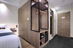 A hotel room with a bed, a wooden wardrobe, a hanging clothes rack, a small shelf with a telephone, and a door with a sign. - Harper Wahid Hasyim, Medan by Aston (Medan)