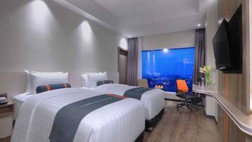 A hotel room with two beds, a desk, a TV, and a view of a cityscape.