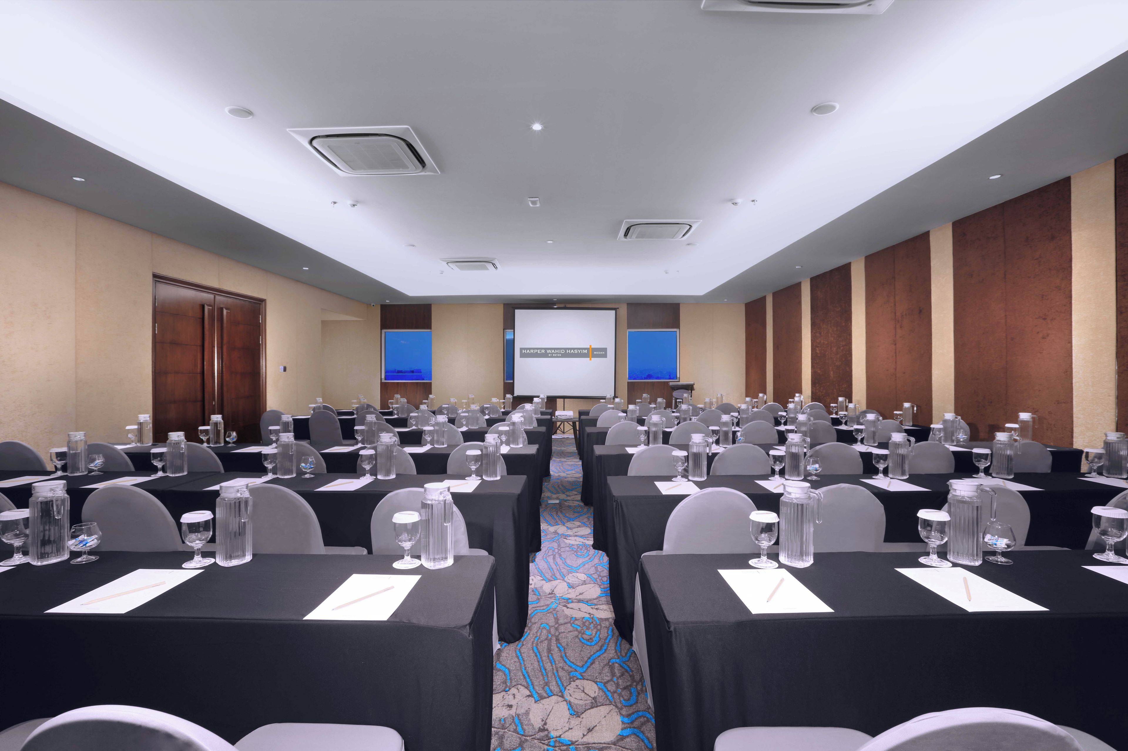 A conference room with rows of tables, chairs, and a presentation screen.