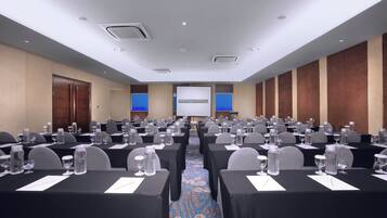 A conference room with rows of tables, chairs, and a presentation screen.