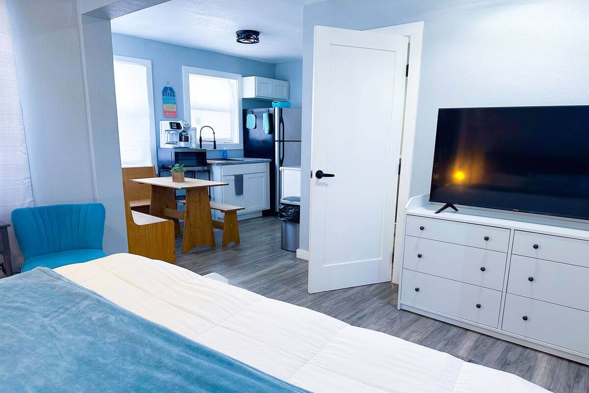 A compact room with a bed, a TV, a small kitchenette, and a dining area.