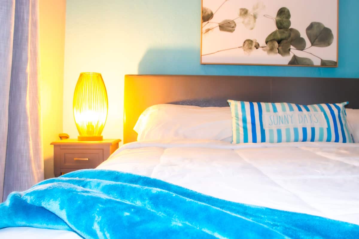 A neatly made bed with a blue and white striped pillow, a bedside lamp, and a wall-mounted artwork.