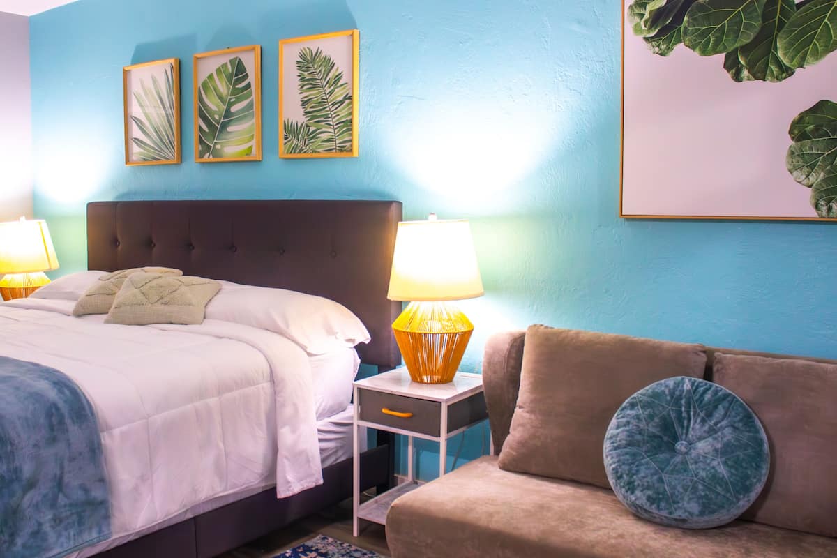A bedroom with a bed, bedside lamps, a nightstand, a sofa, and wall art.