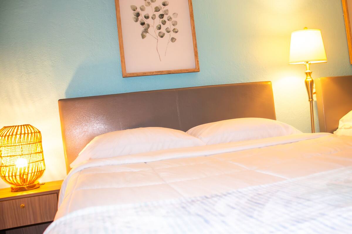 A neatly made bed with white linens, a wooden headboard, and two wall-mounted lamps.