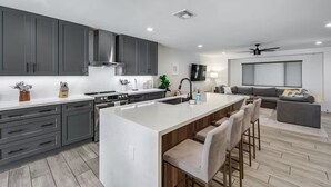 A modern kitchen with grey cabinets, a central island with bar stools, a built-in oven, and a large window.