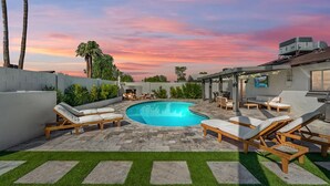 A pool area with lounge chairs and a fire pit, surrounded by a low wall and greenery.