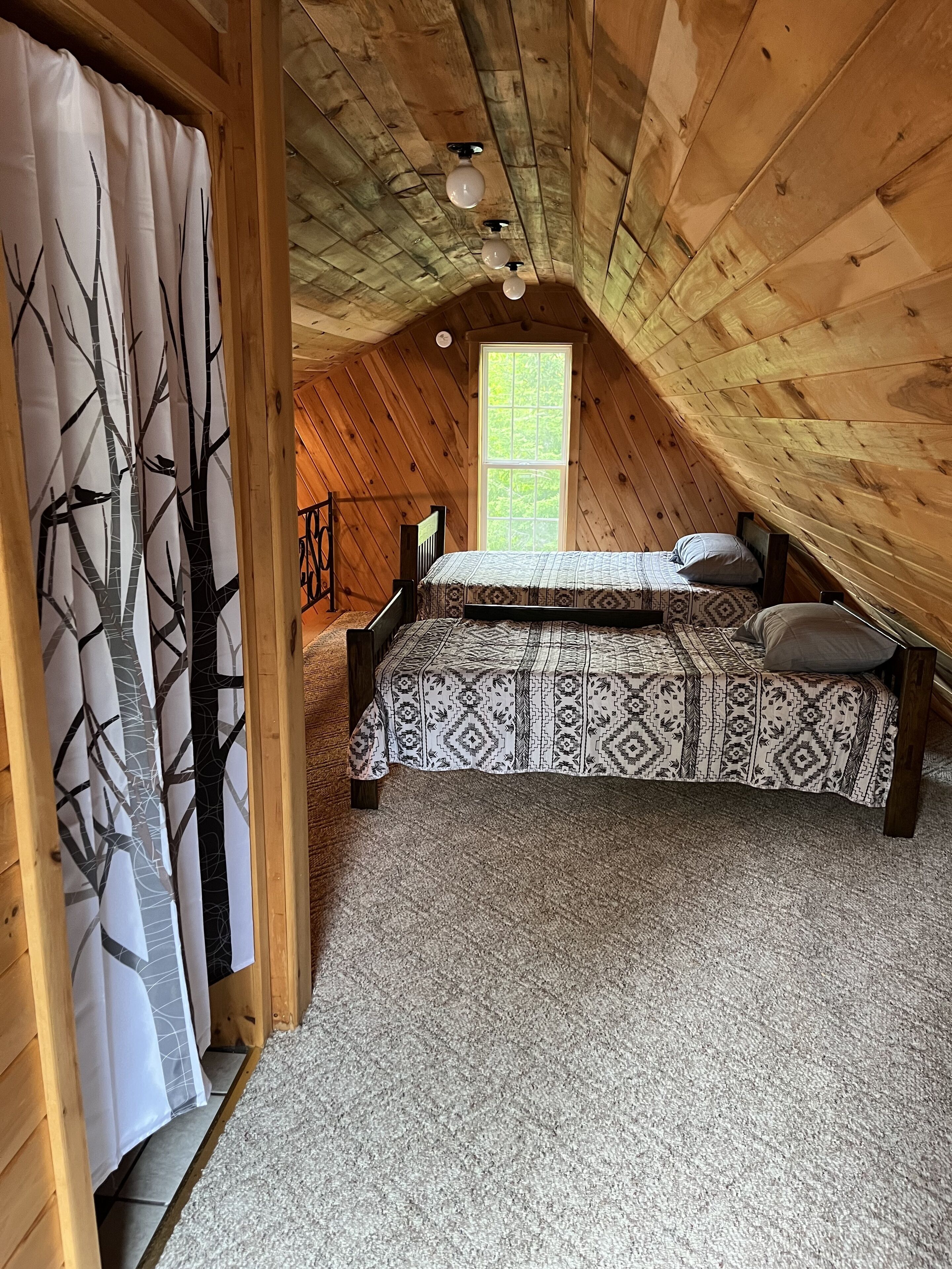 A cozy attic bedroom with a bed, a window, and a view of trees.