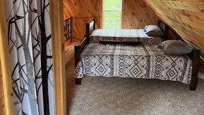 Ein gemütliches Schlafzimmer im Dachgeschoss mit Bett, Fenster und Blick auf Bäume.