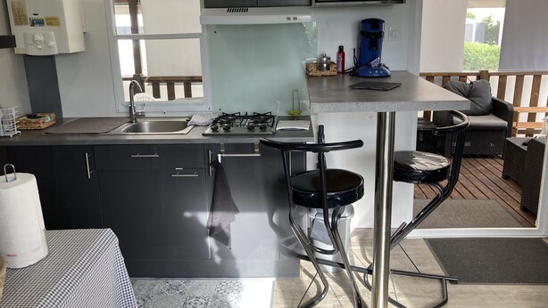 Een kleine keuken met een gasfornuis, een magnetron en een koffiezetapparaat. Er zijn twee barstoelen en een eettafel.