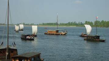 A river with several sailboats, some with passengers, and a docked boat with people on it.