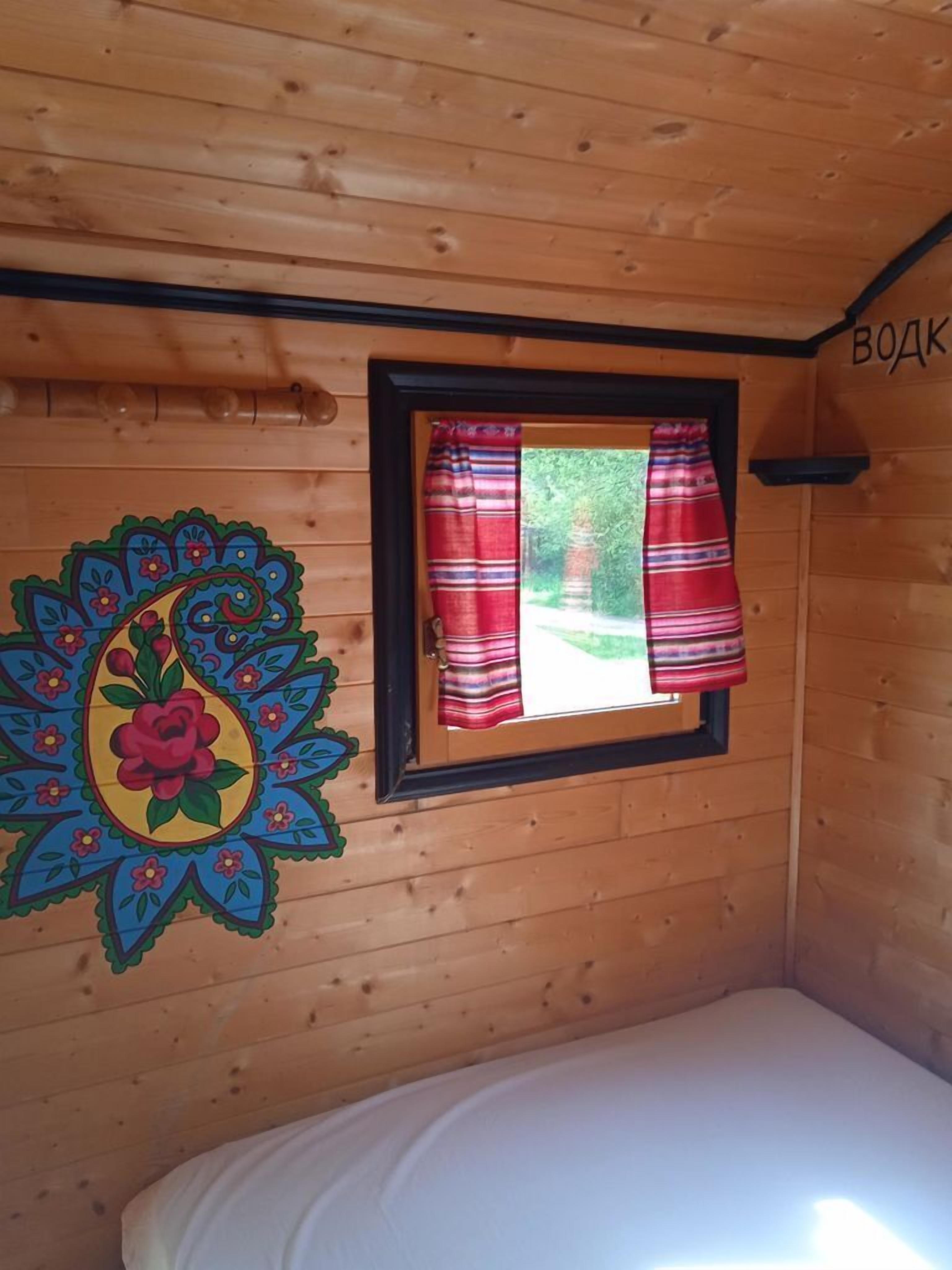 Une pièce de cabane en bois comprenant un lit, une fenêtre avec des rideaux rouges et une décoration murale colorée.