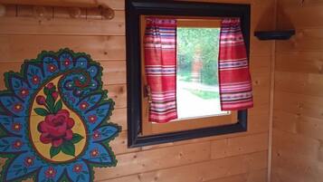 Une pièce de cabane en bois comprenant un lit, une fenêtre avec des rideaux rouges et une décoration murale colorée.