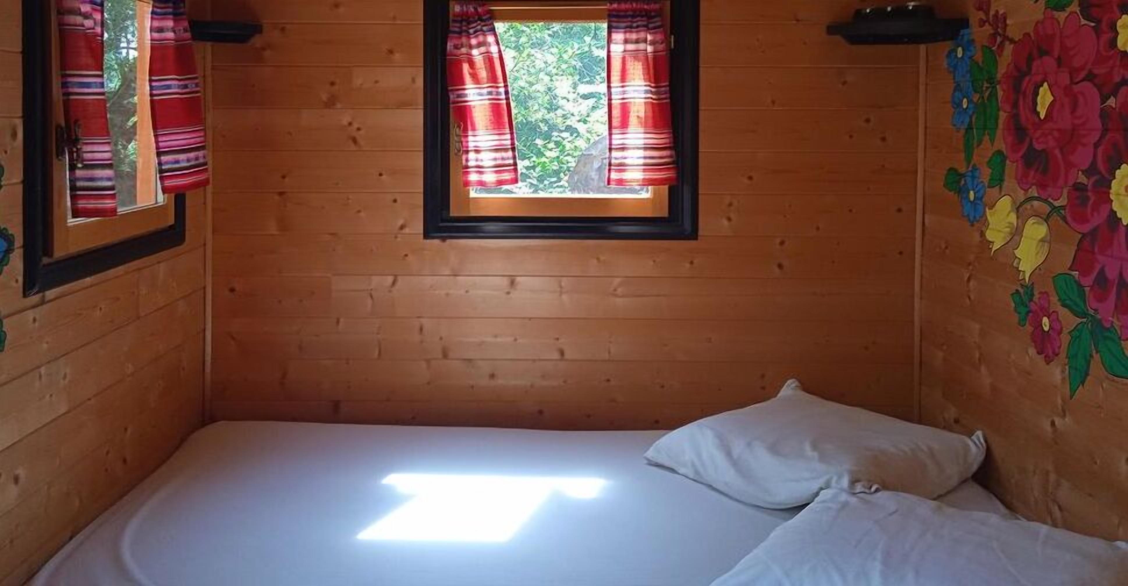 A single bed with white bedding in a wooden cabin room with a window and a floral wall mural.