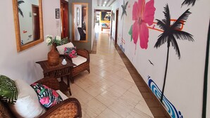 Un couloir doté d’un sol carrelé, de meubles en osier et d’une fresque murale représentant des fleurs tropicales et des palmiers.