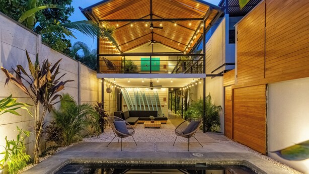 Une maison moderne dotée d’un patio couvert, d’une piscine et d’une grande porte en bois.