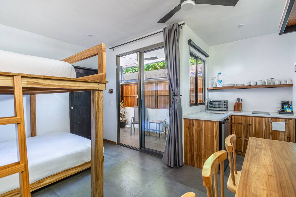 Habitación compacta con literas, kitchenette y puerta corrediza de vidrio que da a un patio exterior.