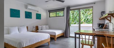 Una habitación de hotel moderna con dos camas individuales, un escritorio de madera con una silla, un ventilador de techo y un ventanal con vistas a zonas verdes.