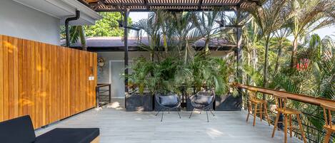 An outdoor patio with wooden flooring, a black sofa, and wooden tables and chairs.