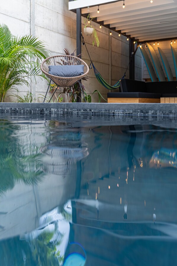 Un área de piscina con una silla de mimbre, una hamaca y un muro de hormigón.